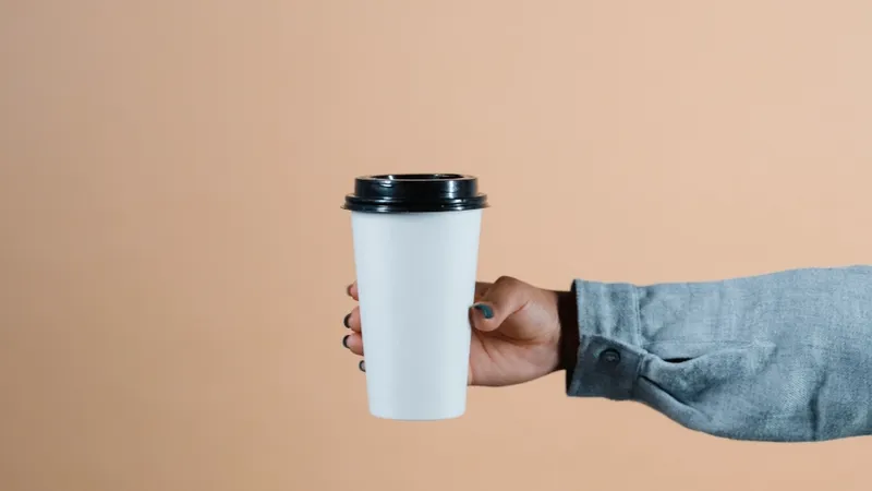 Person's hand holding a disposable mushroom coffee cup against a beige background.